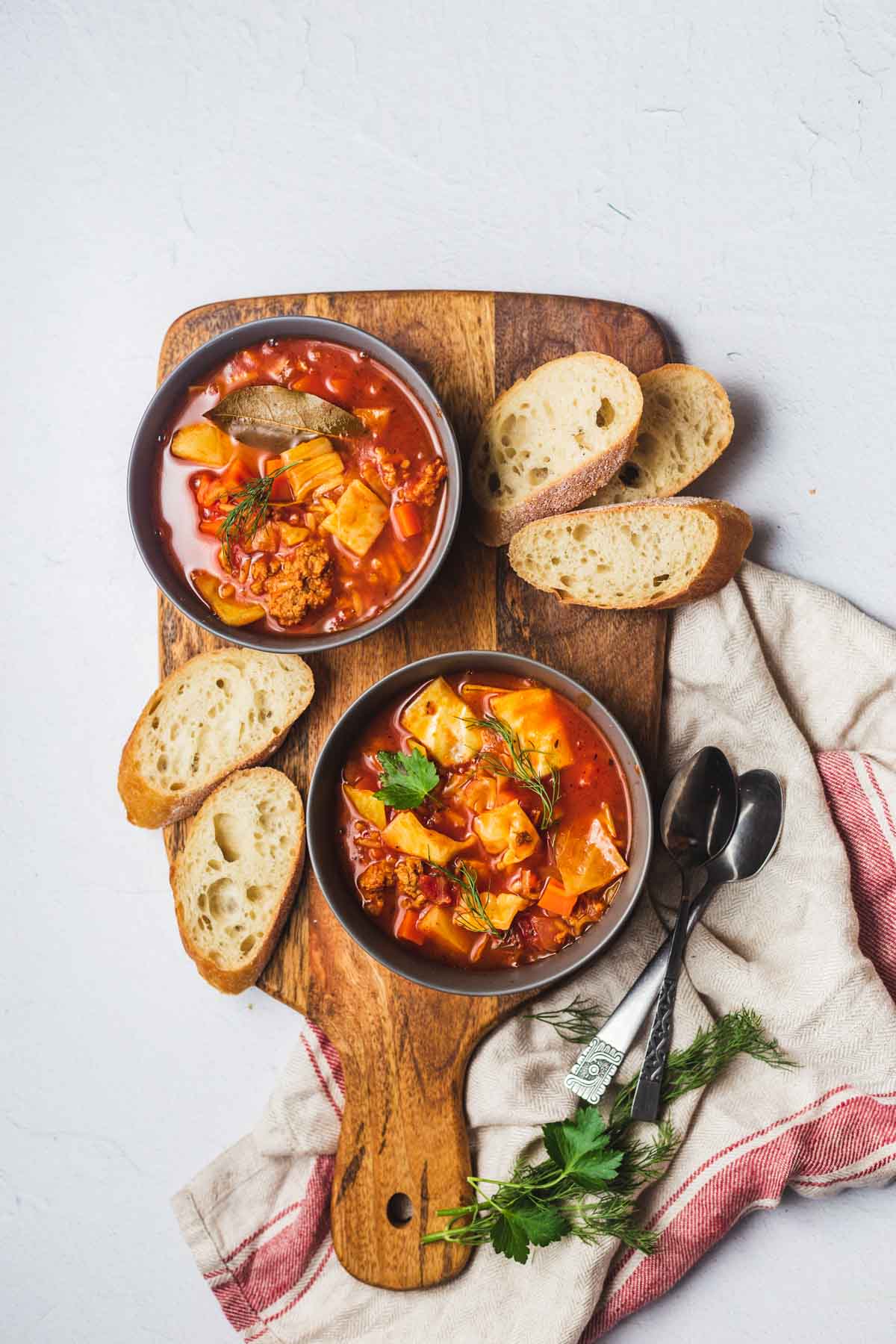 Birds eye view image of two bowls with unstuffed cabbage roll soup on a wooden board served with bread.