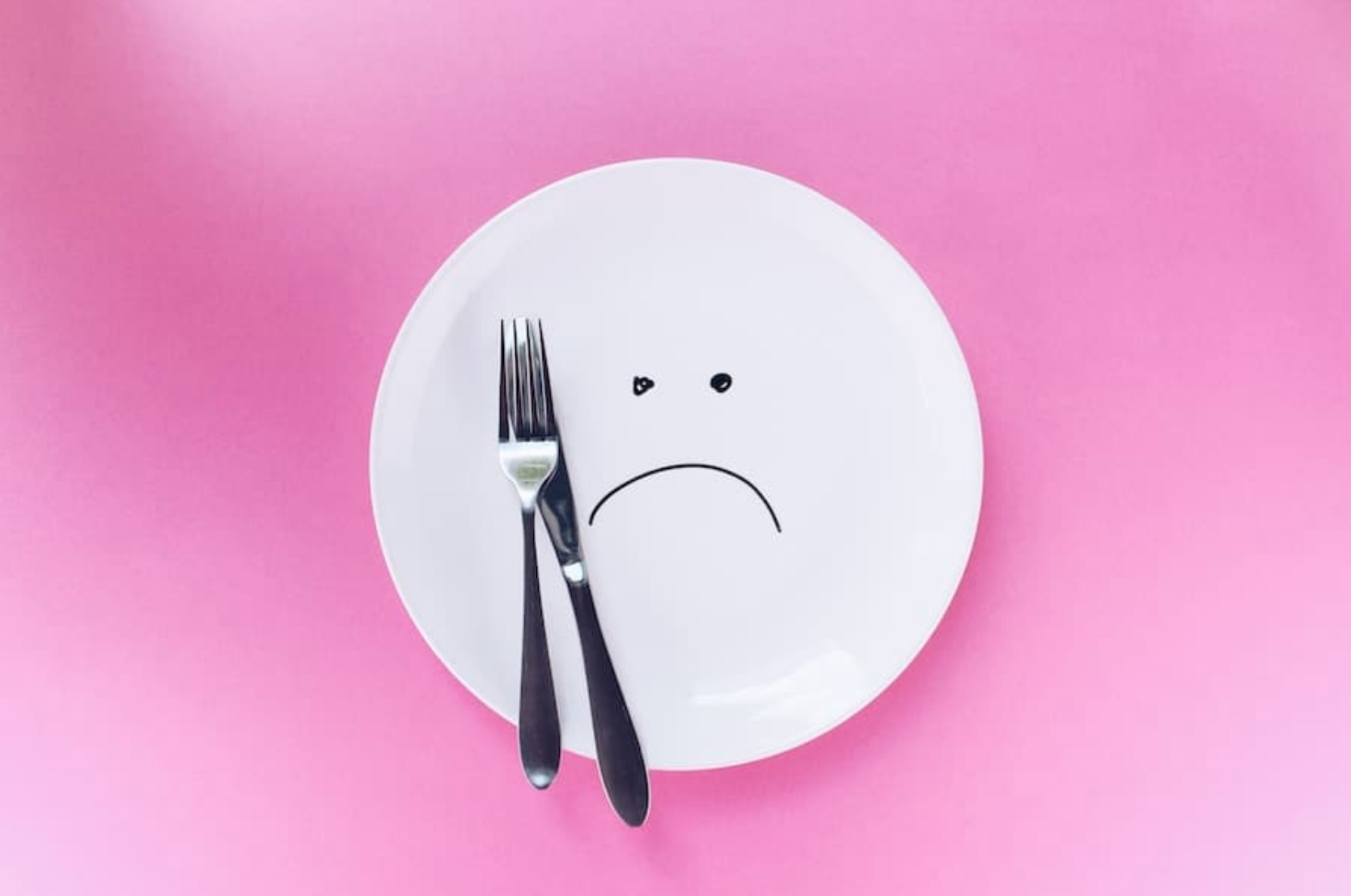 White plate with a sad face on a pink background.