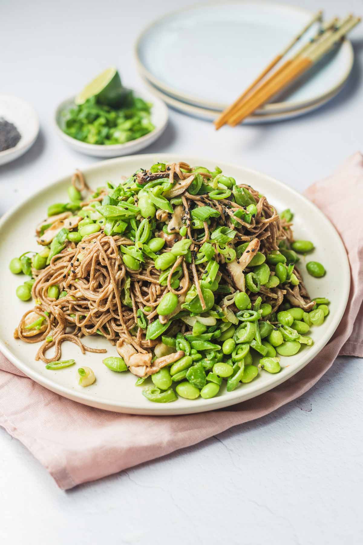 Up close view of miso pasta on a white plate with plates, ingredients, and chop sticks in the background.