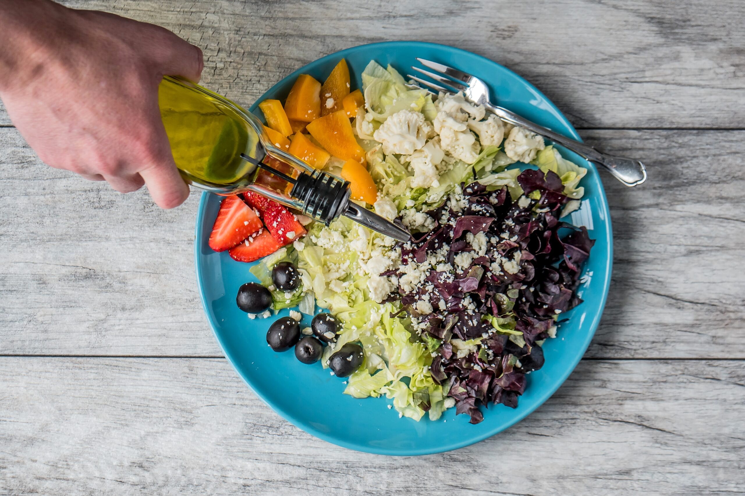 Olive oil being poured on a salad with cheese and olives to help gain weight.