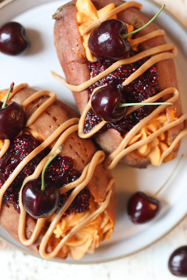 Birds eye view of vegan stuffed sweet potatoes with PB&J on top and cherries on a white plate.