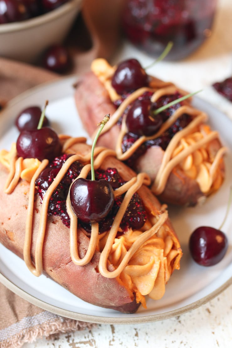 Up close picture of 2 vegan stuffed sweet potatoes with PB&J and a cherries on top. 