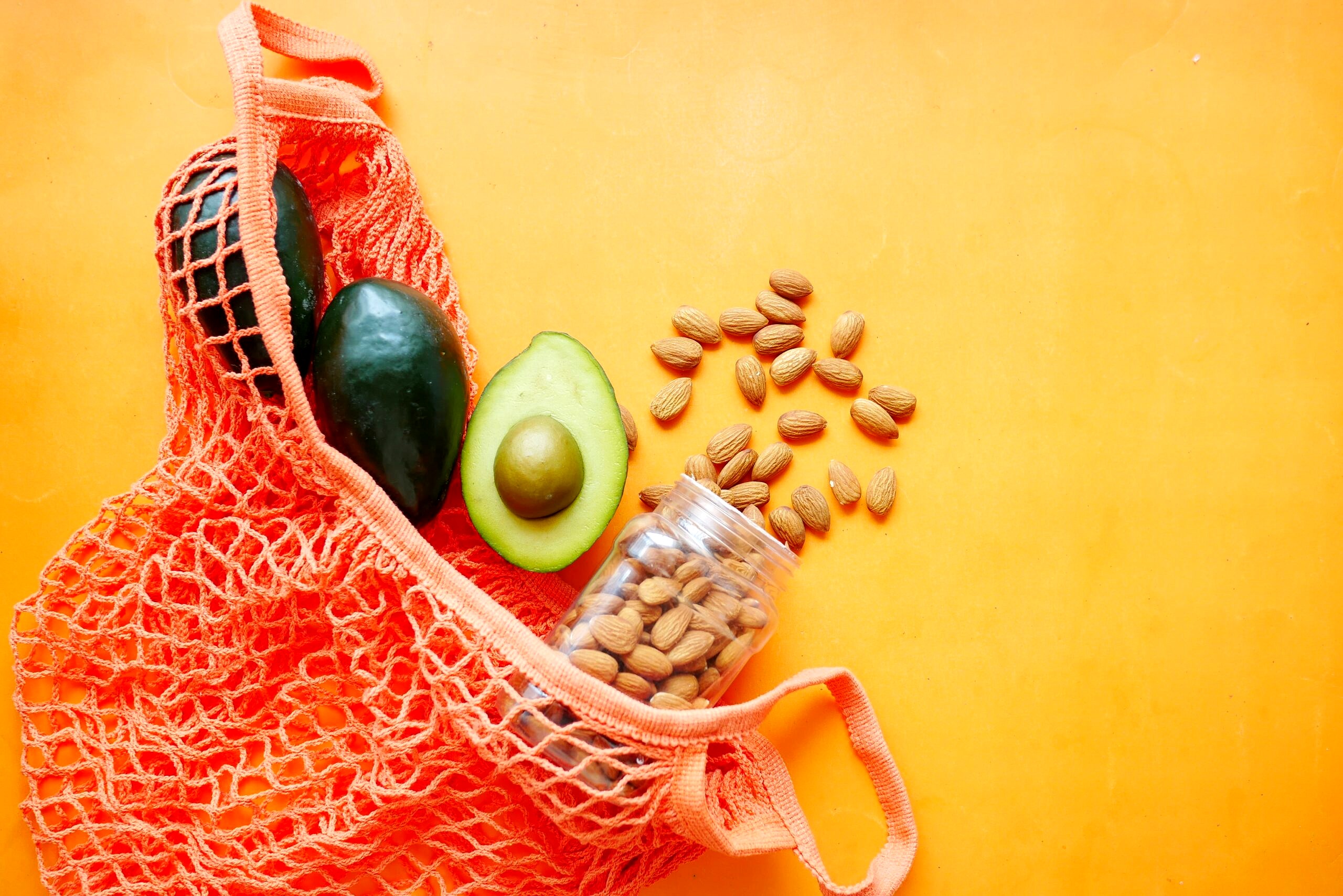 Avocado and almonds in a red bag on an orange background.