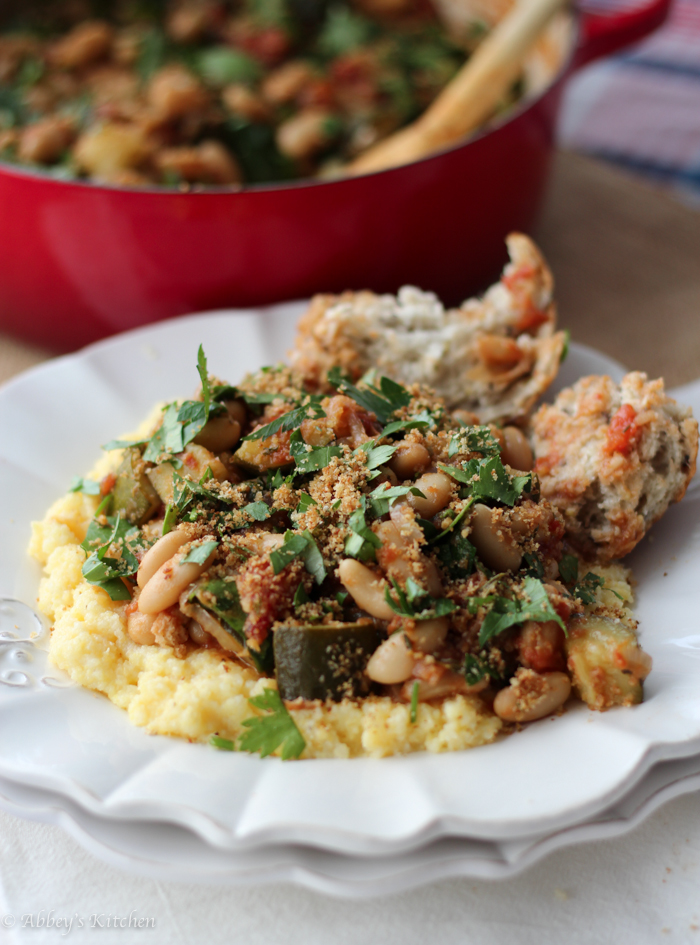 up close view of cassoulet on a bed of polenta on a white plate with a red dutch oven with cassoulet inside in the background