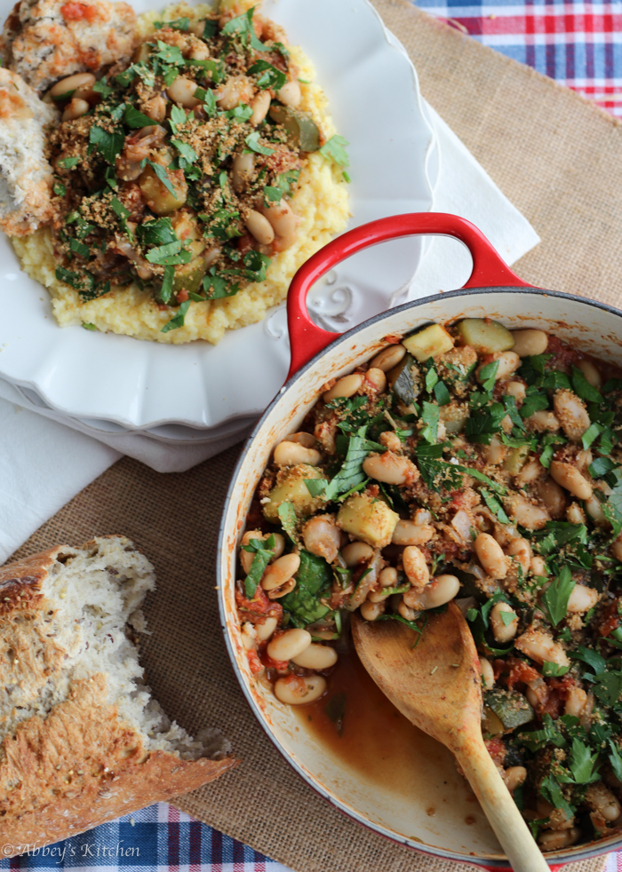 Birds eye view of cassoulet on a bed of polenta at top, cassoulet in a dutch oven on the right, and a baguette on the left.