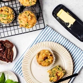 Birds eye view of savoury muffins on a cooling rack and on a plate next to butter and a knife.