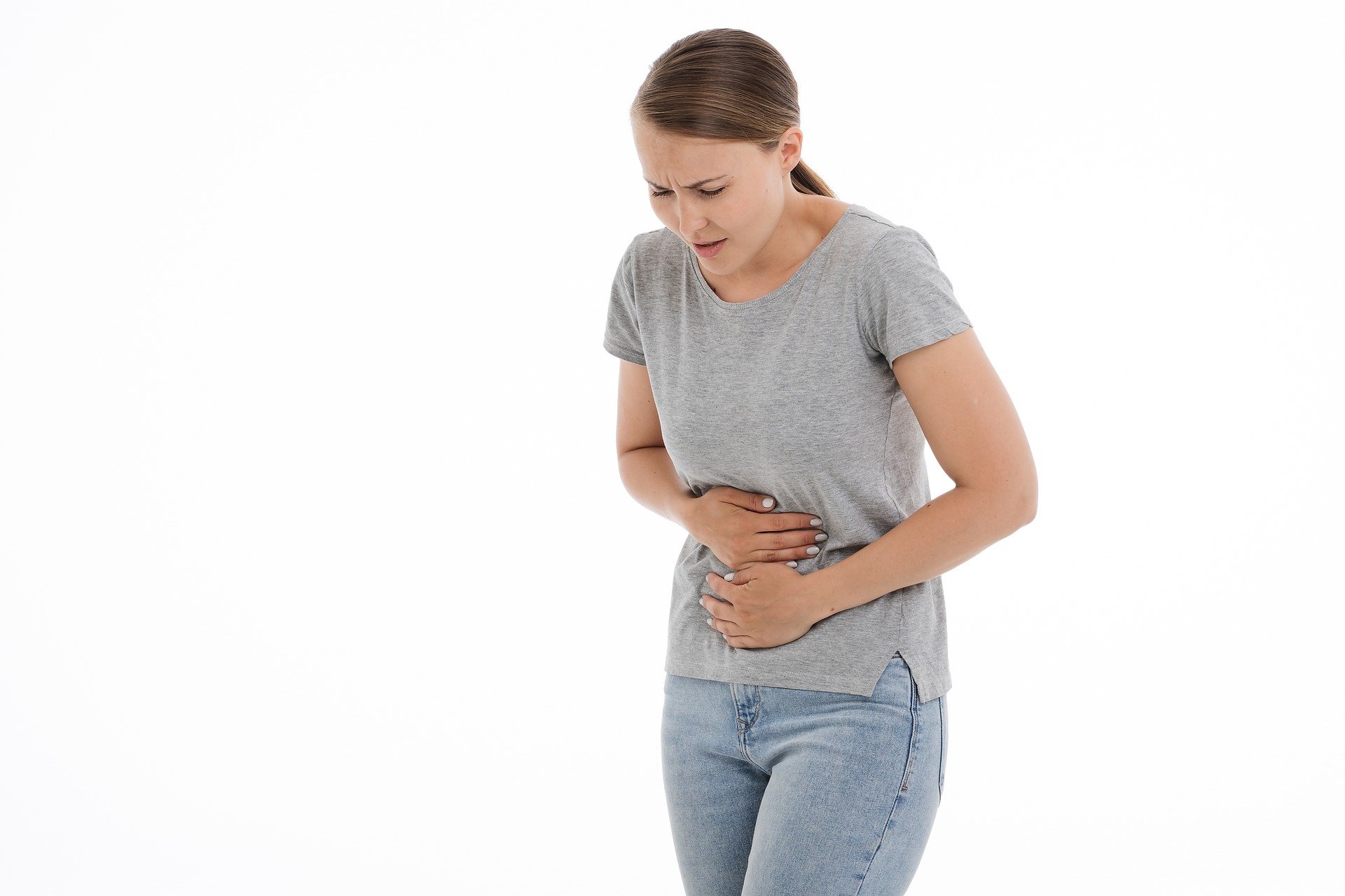 A girl in a grey shirt holding her stomach in pain.