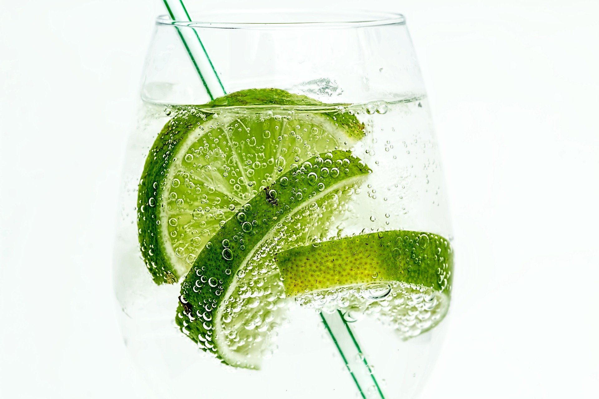 A glass with carbonated water, limes, and a white and green straw inside.