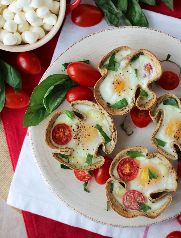 Birds eye view image of veggie egg muffins with tomatoes and basil on a plate.