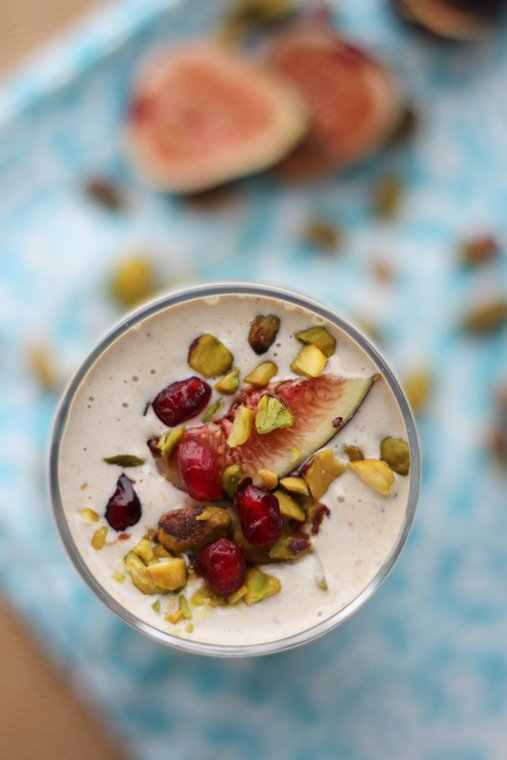 An overhead image of a glass of smoothie that is topped with pistachio, pomegranate seeds, and fig.