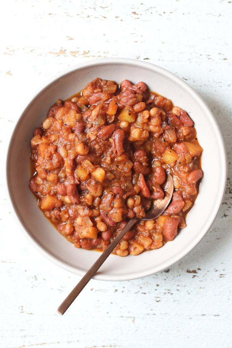 Birds eye view of vegan baked beans in a white bowl with a spoon in the disk. 