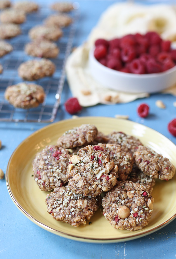 A picture of the peanut butter and jelly cookies on a yellow plate, with a blurred background involving a bowl of raspberries and a baking tray with the cookies.