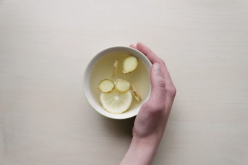 Hand holding mug with water and ginger.
