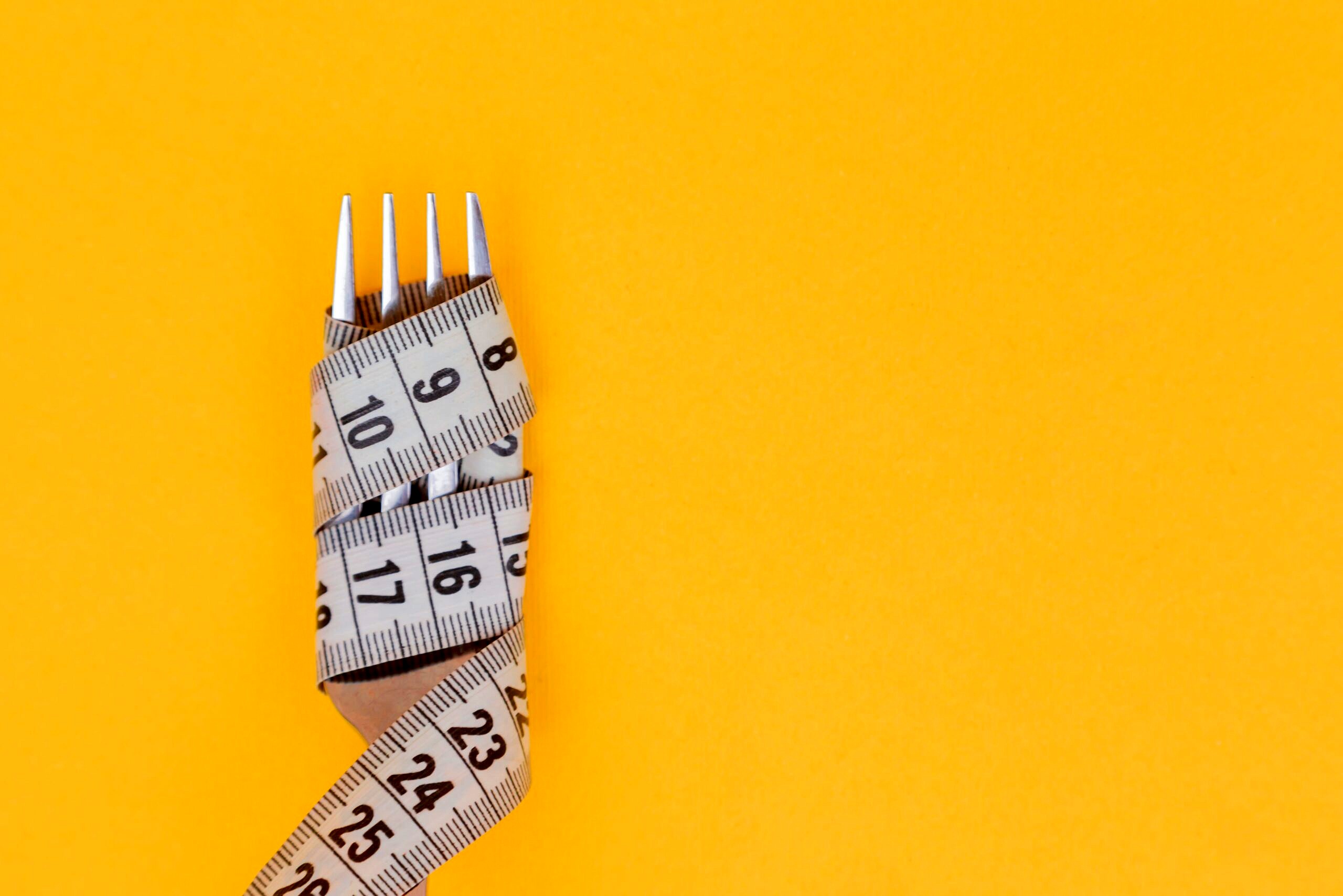 Fork and tape measure against a yellow background.