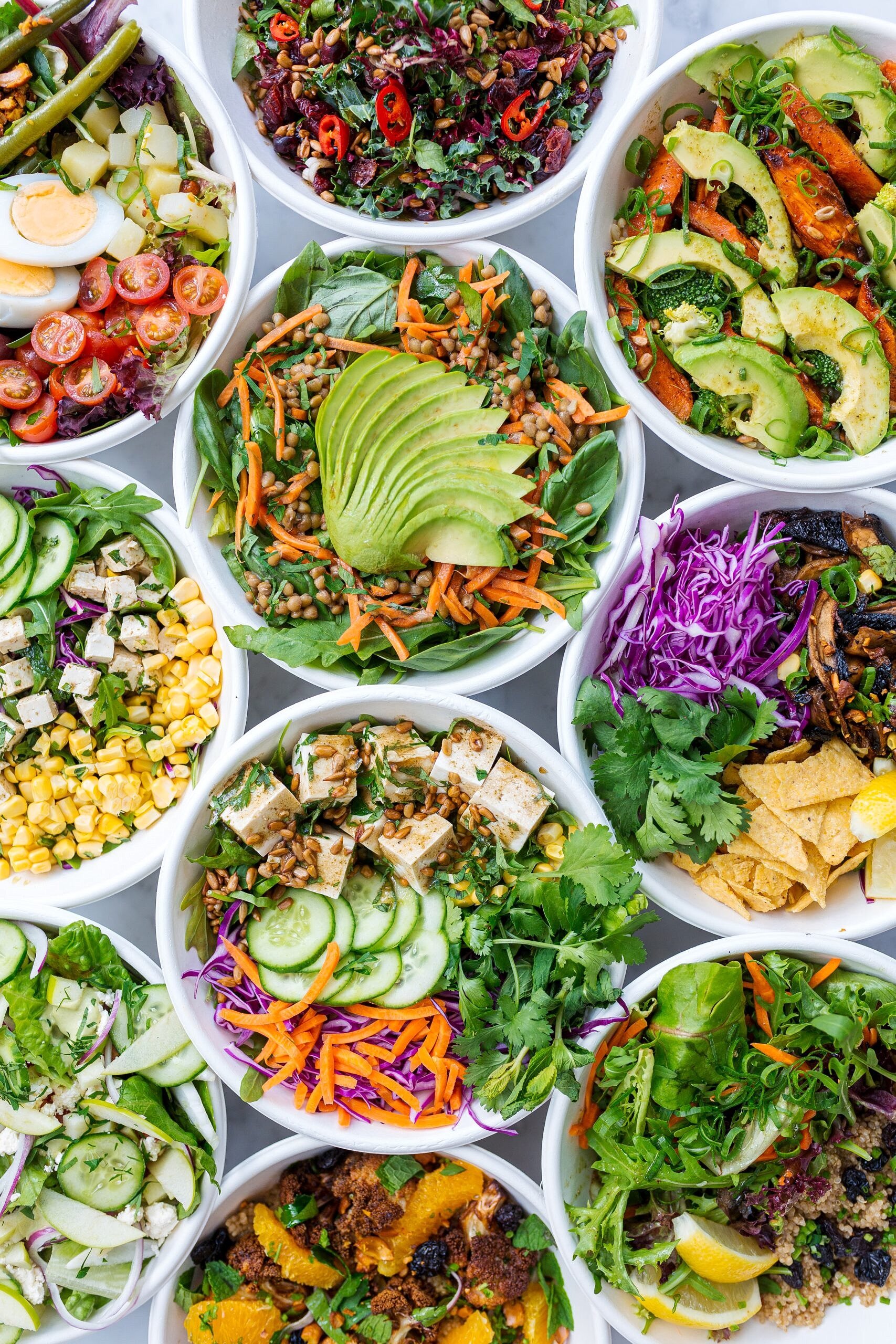 Birds eye view image of multiple salads in white bowls.