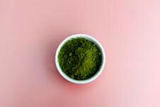 Greens powder in a white bowl against a pink background.