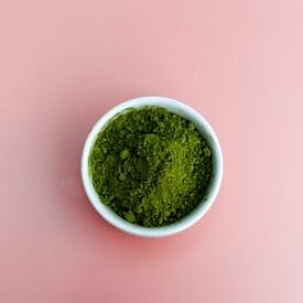 Greens powder in a white bowl against a pink background.