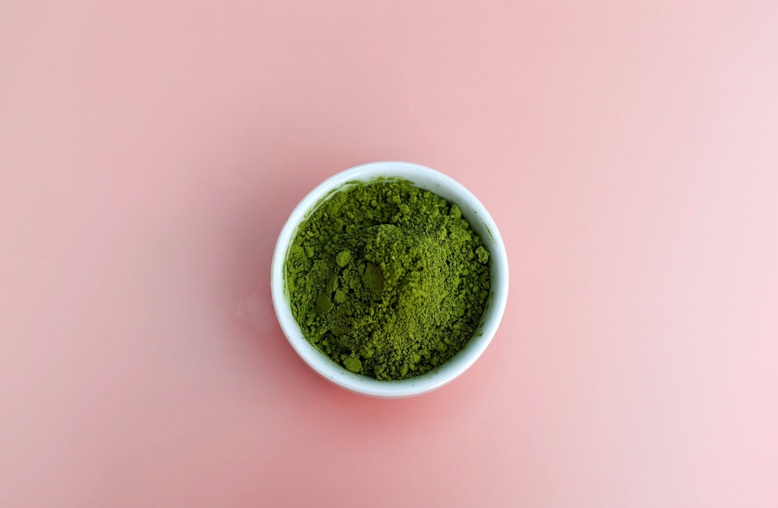 White bowl with greens powder against a pink background.