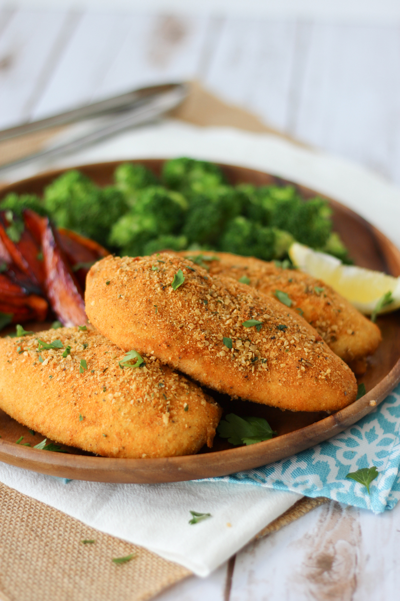 3 shake and bake chicken breasts on a brown plate with sweet potato fries, broccoli, and a lemon wedge.