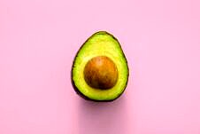 Half of an avocado against a pink background.