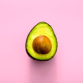 Half of an avocado against a pink background.