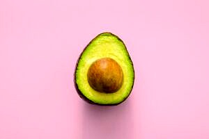 Half of an avocado against a pink background.