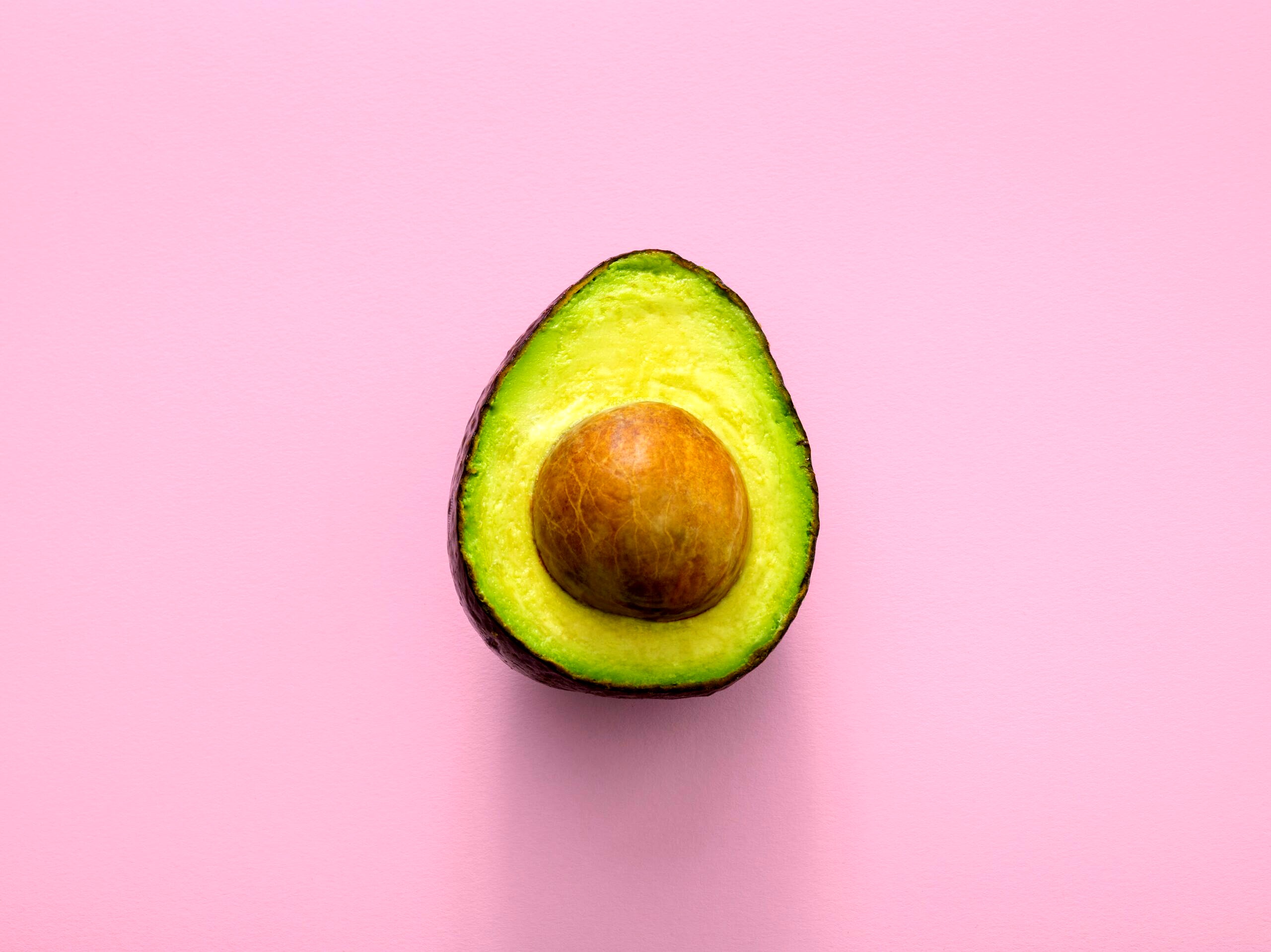 Half of an avocado against a pink background.