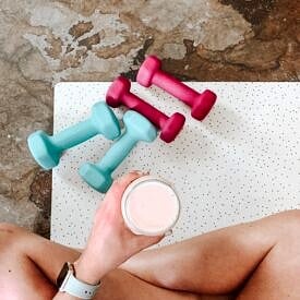 Person holding a sports drink during exercise on a mat with dumbbells.