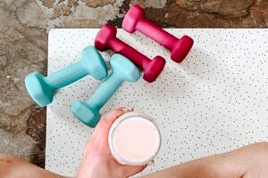Person holding a sports drink during exercise on a mat with dumbbells.