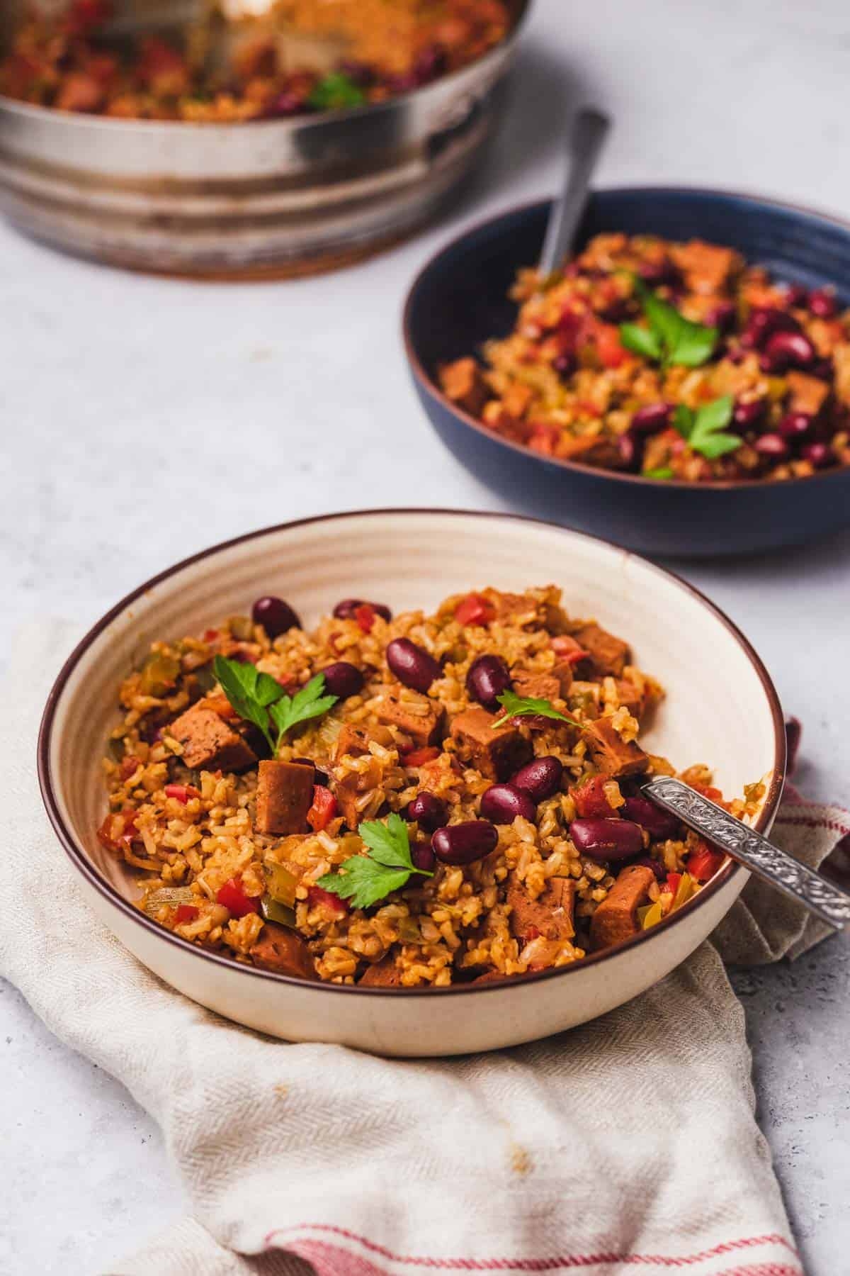 Picture of 2 bowls of vegan jambalaya, the closer bowl is white bowl and the further bowl is blue. 