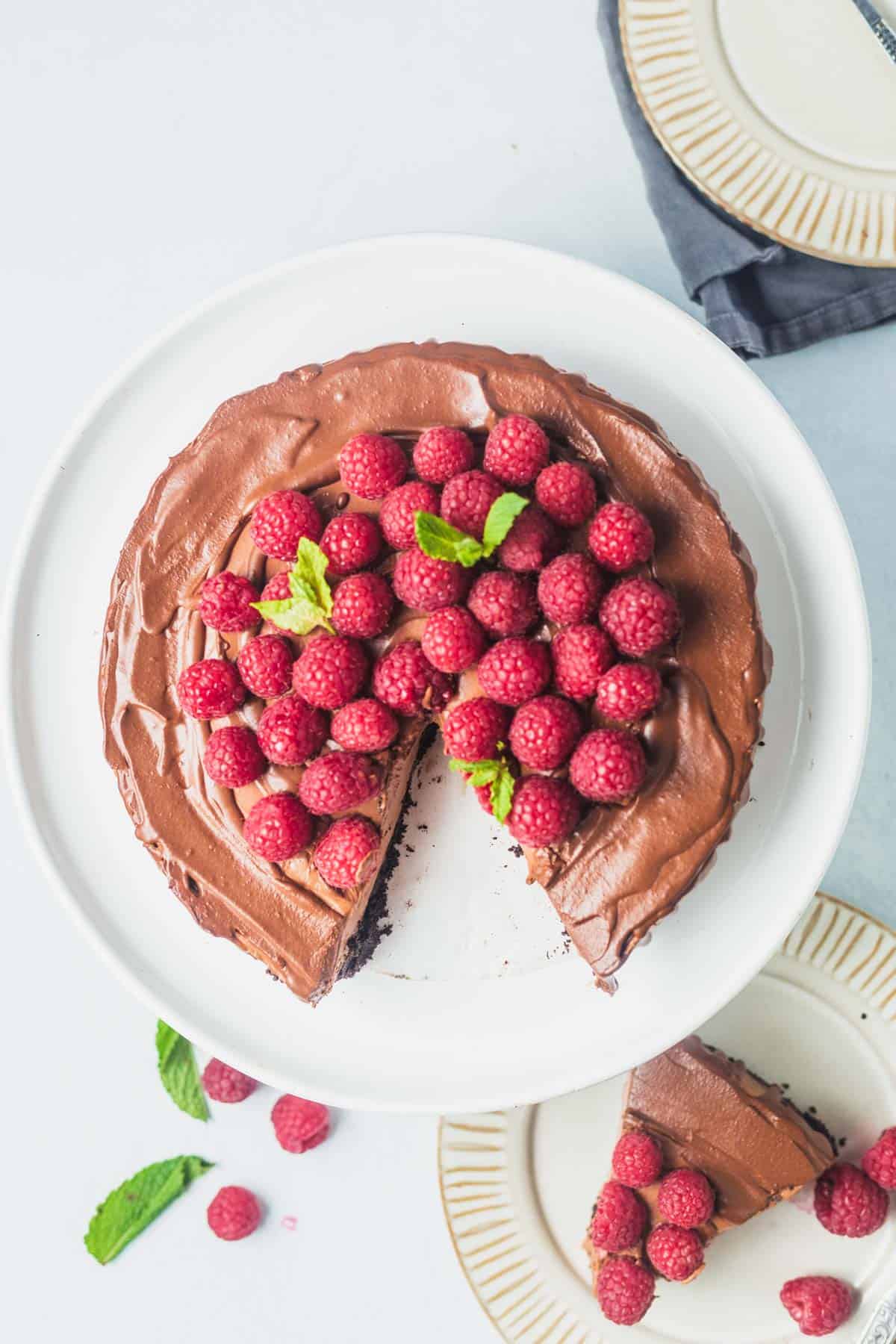 Birds eye view of chocolate tofu cheesecake with chocolate and oreos on a plate with raspberries.