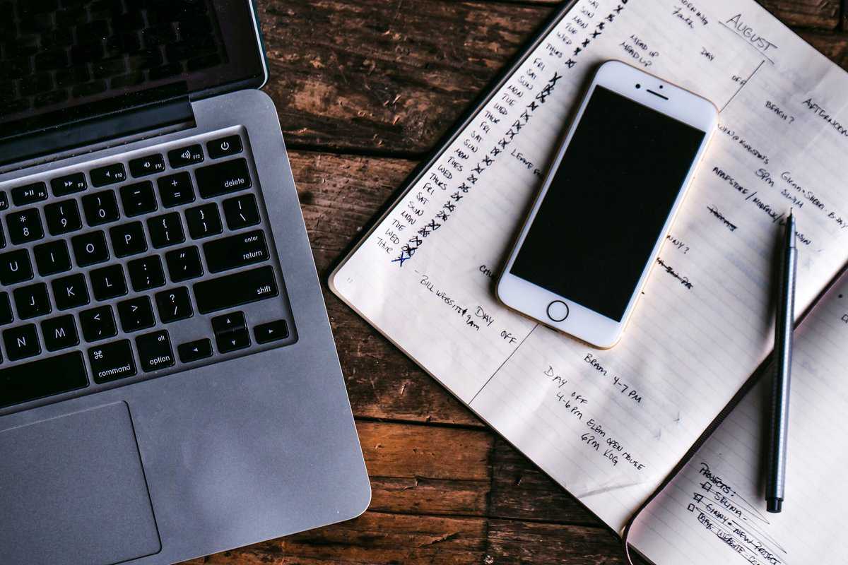 Laptop, phone, and schedule on a wooden table.