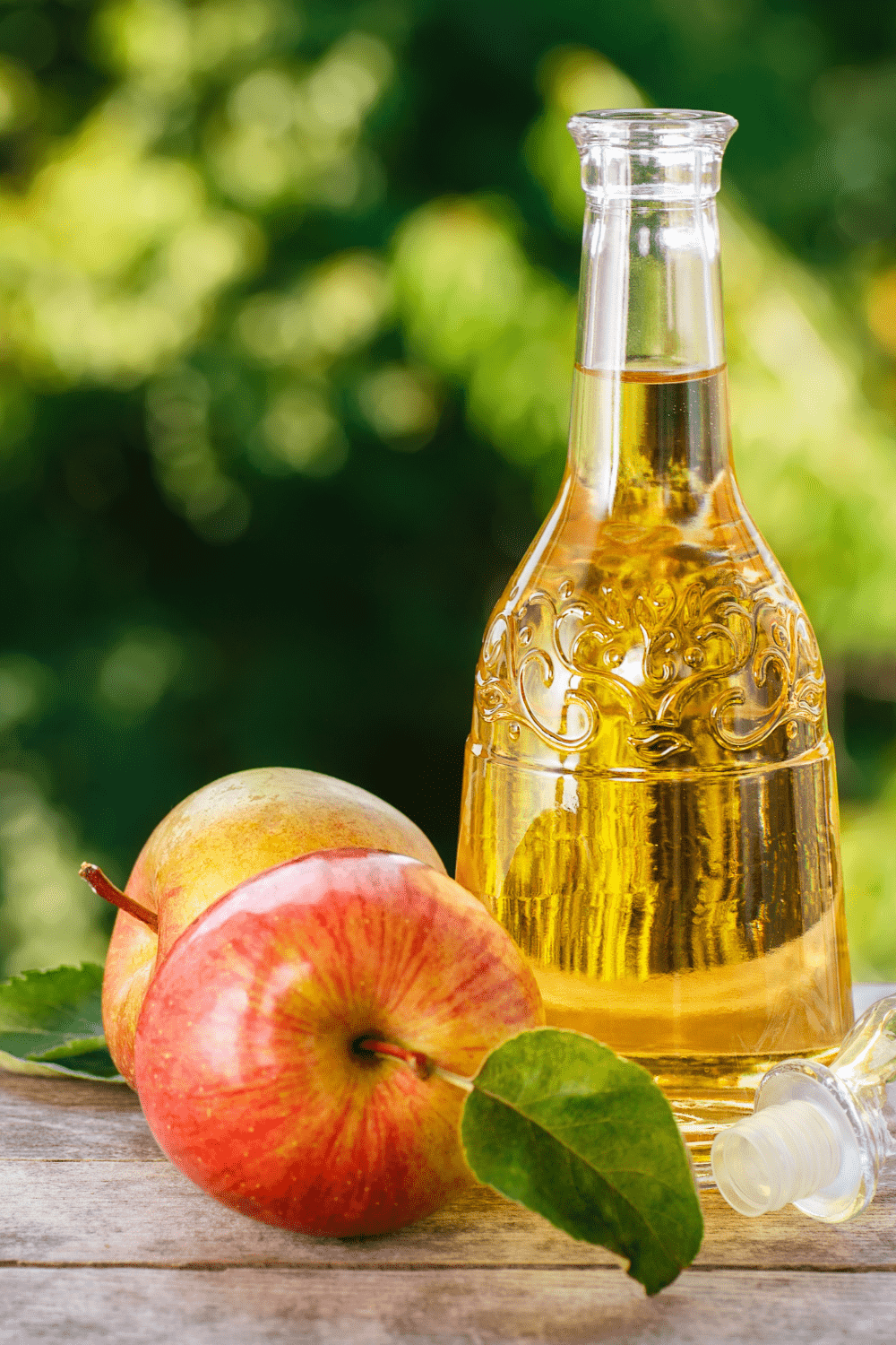 Picture of 2 apples on the left and a clear bottle of apple cider vinegar on the right.
