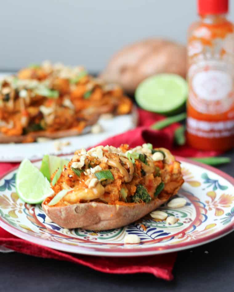 Picture of chicken satay with peanut sauce & sweet potatoes on colorful patterned plate with a bottle of sriracha in the background.