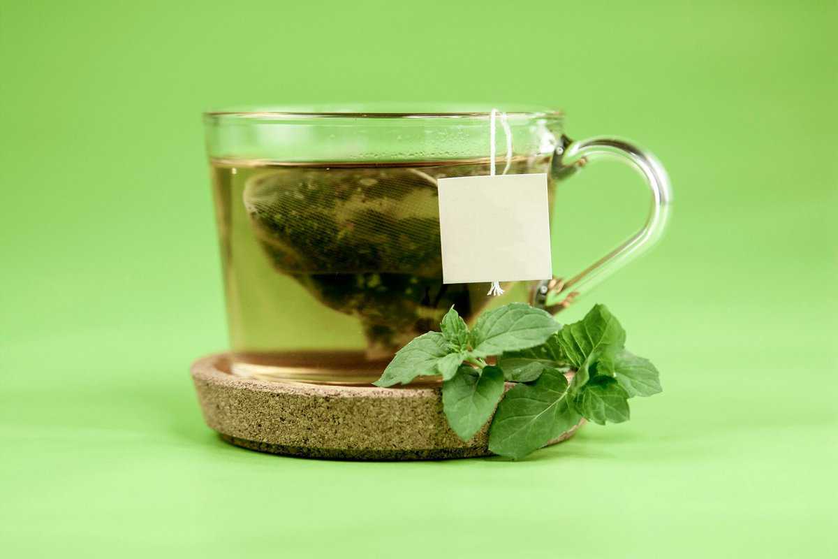 Close up of a clear glass mug with green tea leaves presented as an example for foods that promote heart health.