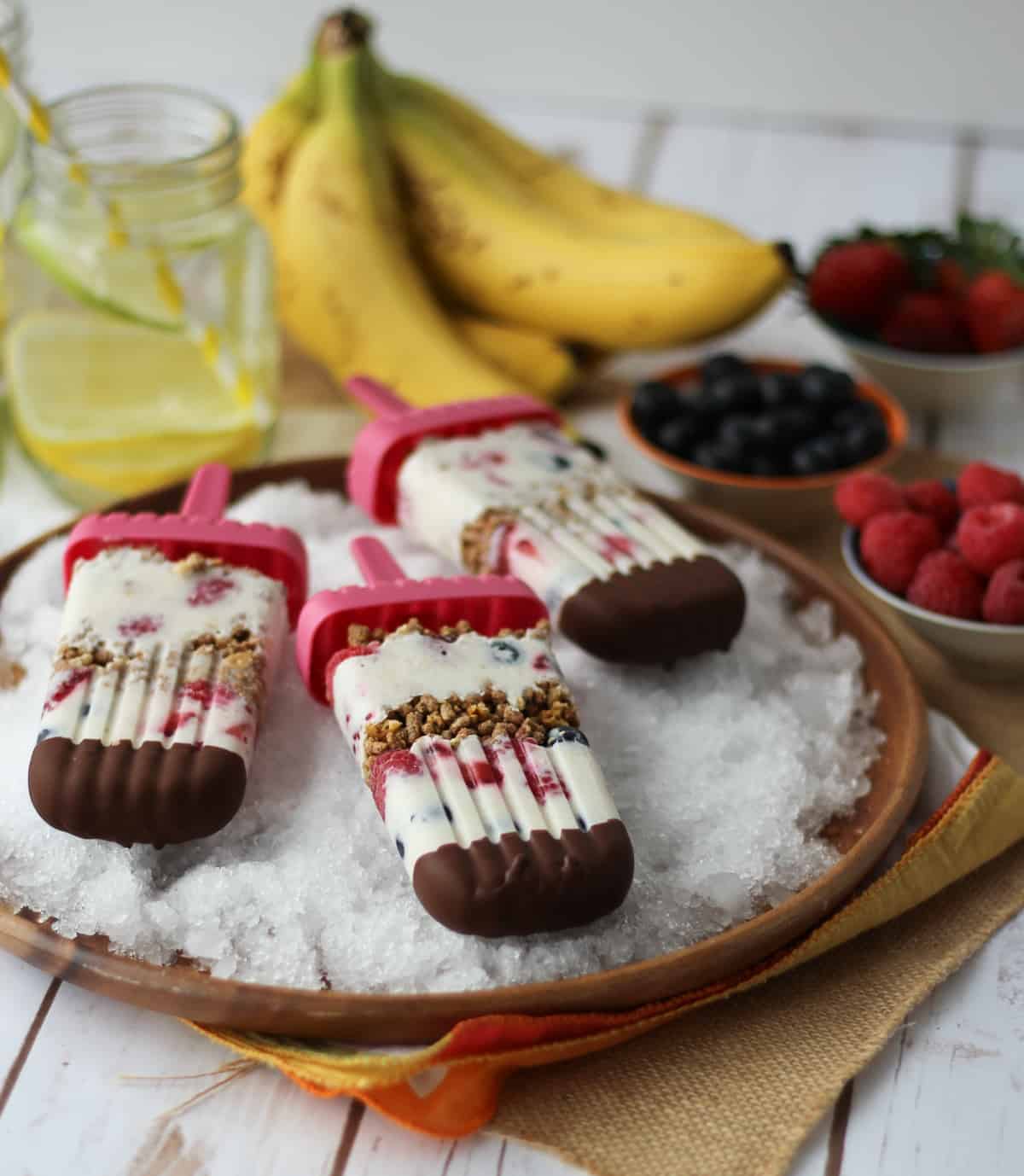 3 banana popsicles on ice with fruits in the background