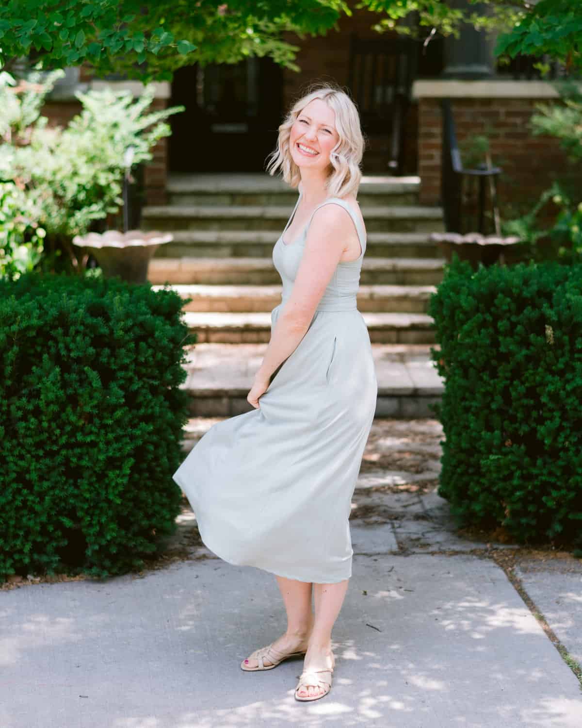 Abbey standing in front of a house, wearing a light gray dress and smiling.