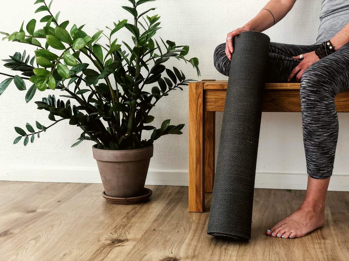 Woman holding a yoga mat and sitting on a bench.