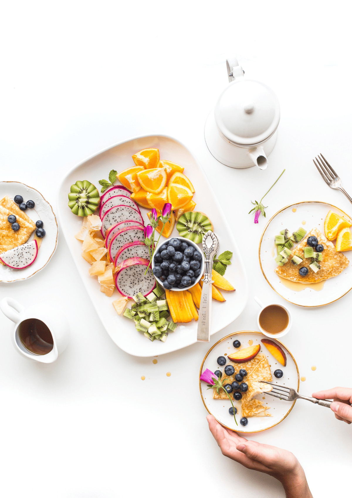 Birds eye view of a 4 plates of fruit and crepes and 2 tea cups.