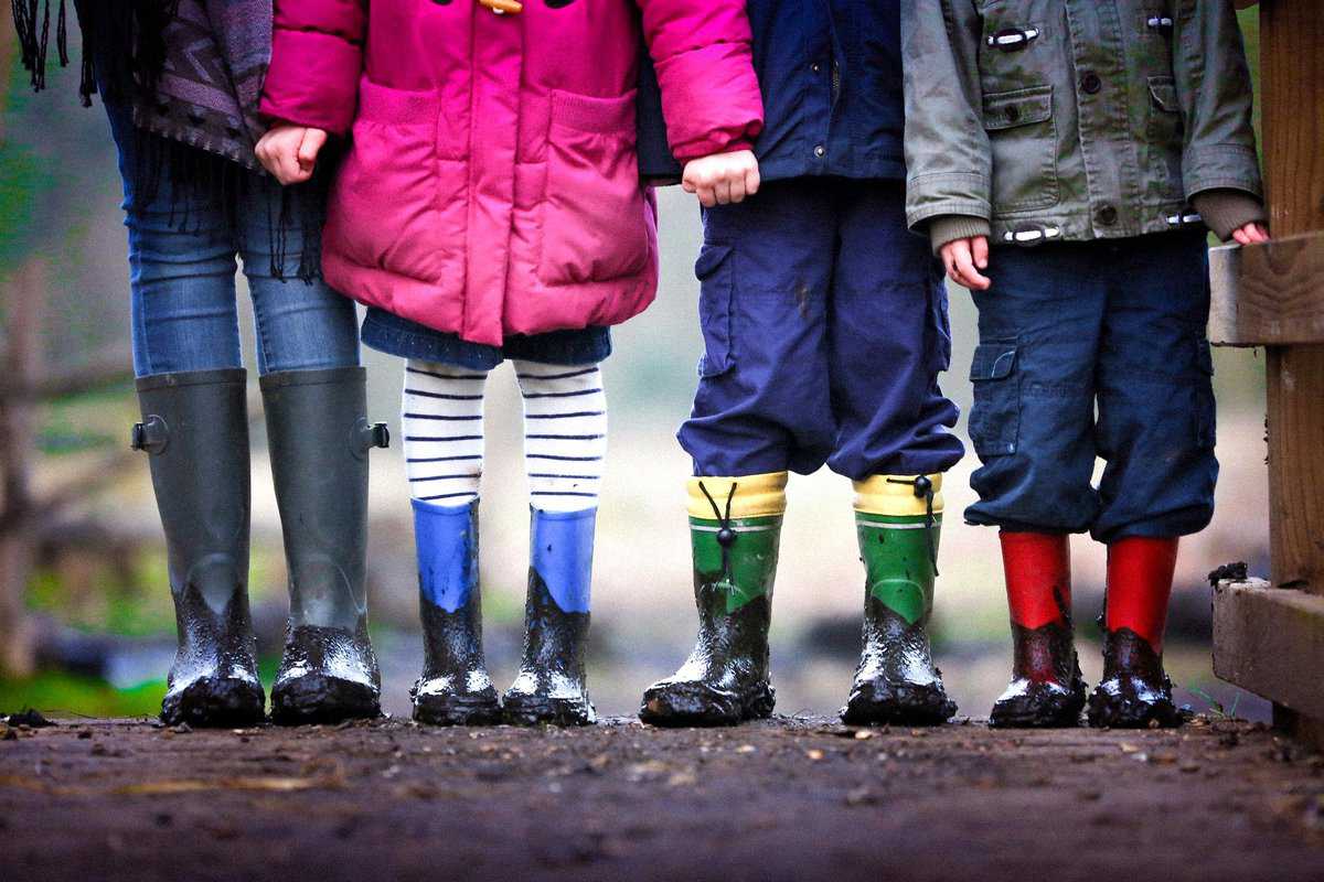 Four kids in coats and rain boots holding hands.