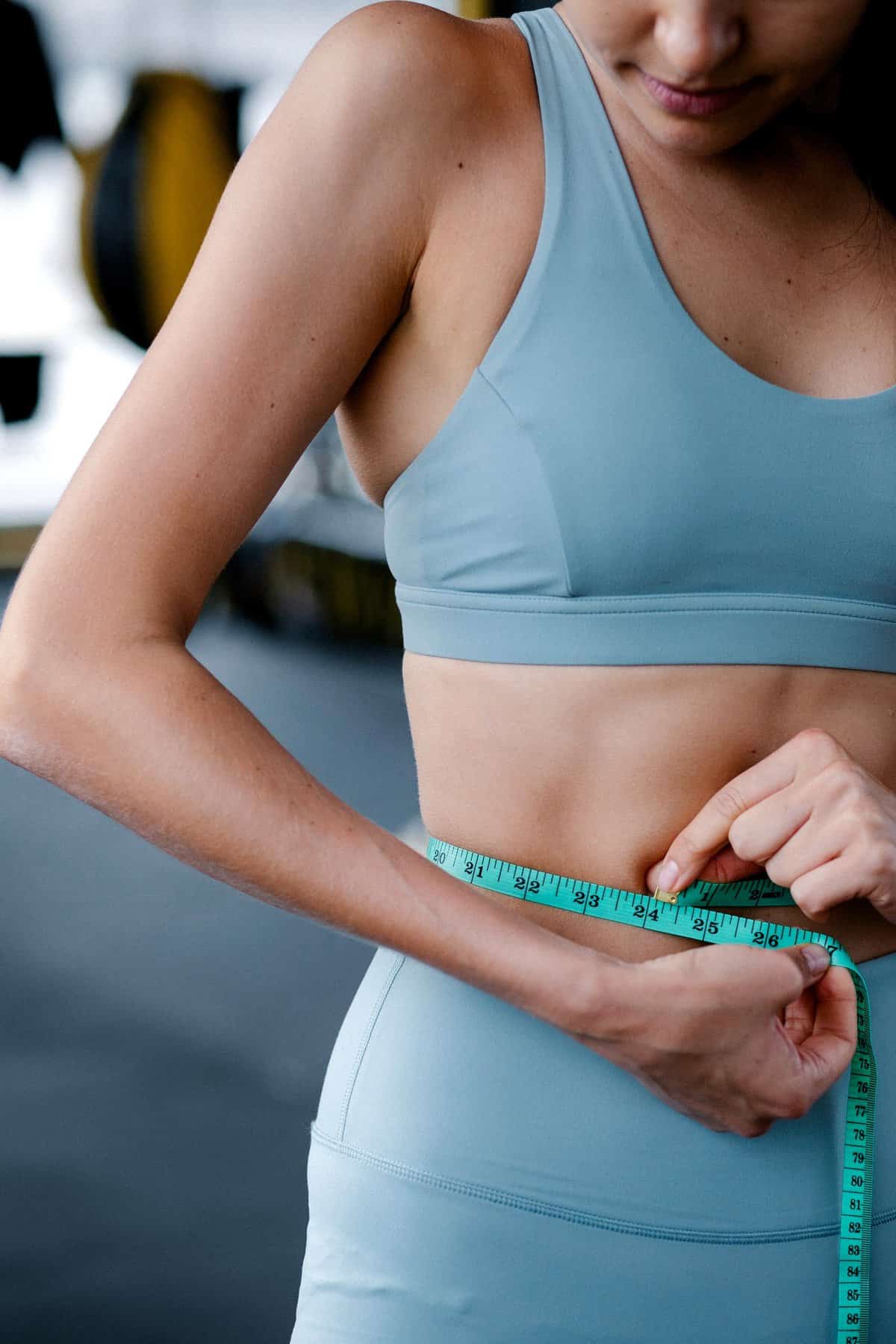 Woman in workout set measuring waist with a measuring tape.