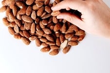 Hand reaching for one almond from a pile.