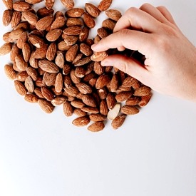 Hand reaching for one almond from a pile.