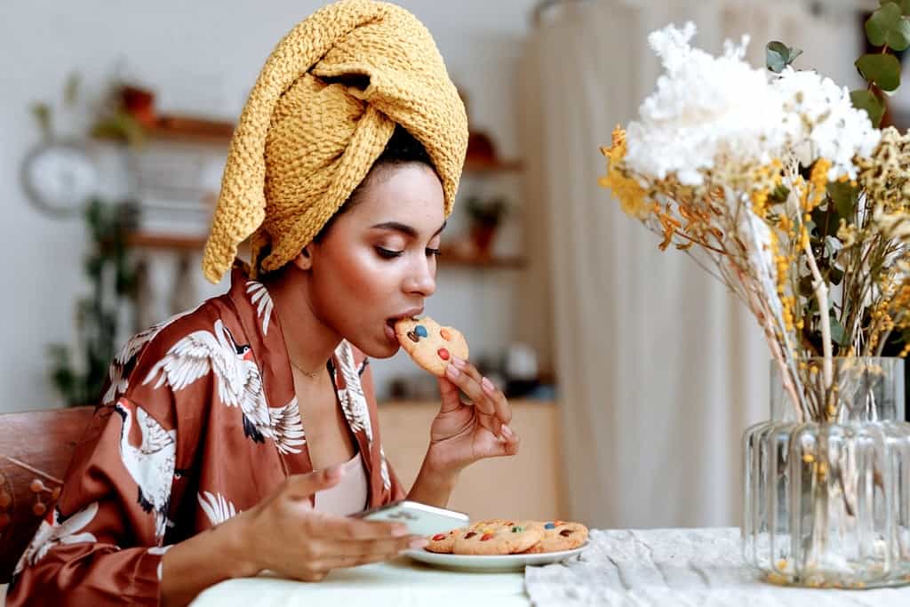 Woman eating a cookie while scrolling on her phone.