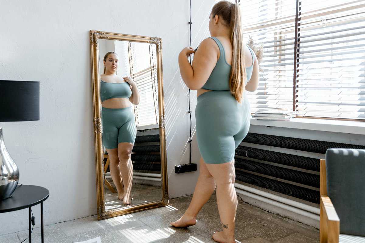 Woman in a workout outfit looking at her body in the mirror.