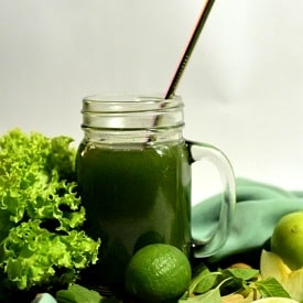 Glass mug of AG1 greens next to kale, limes and other green produce.