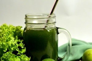 Glass mug of AG1 greens next to kale, limes and other green produce.