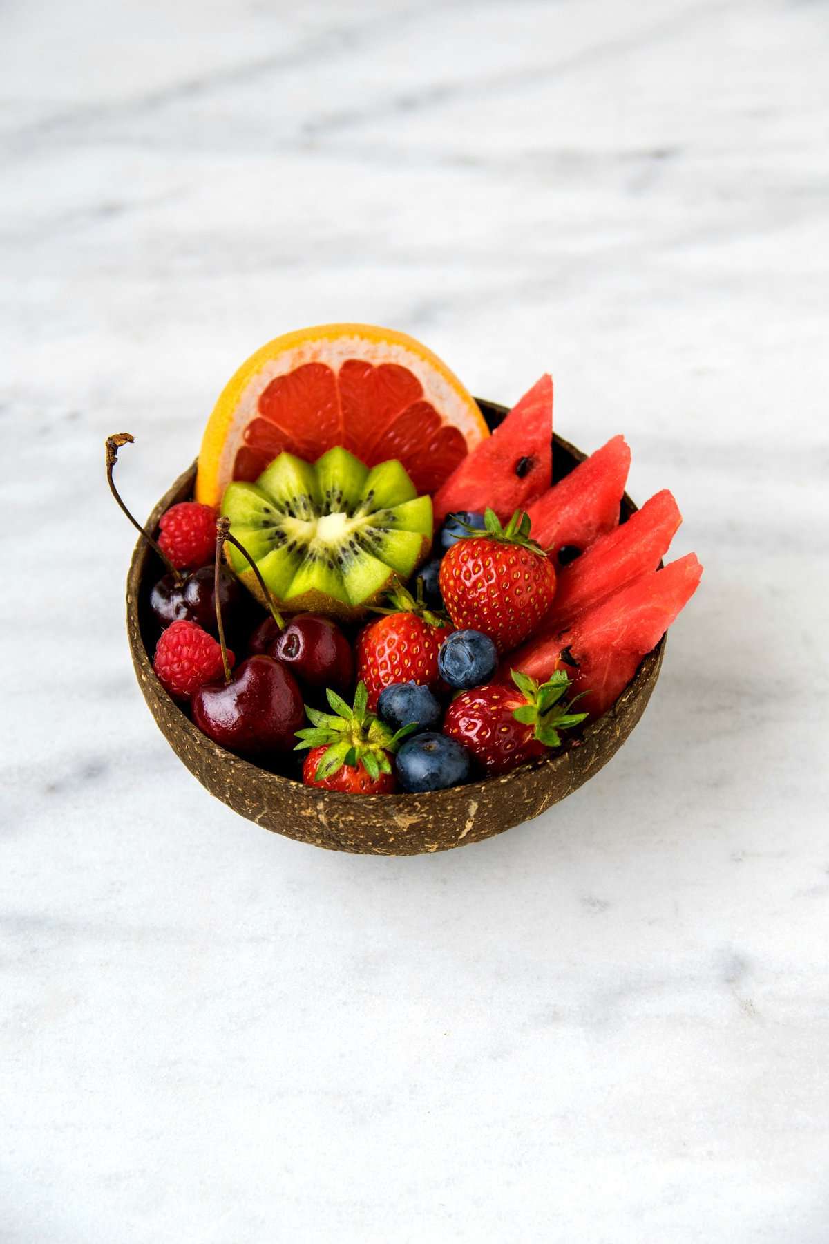 Brown coconut bowl with kiwi, berries, watermelon, grapefruit and other various fruits.