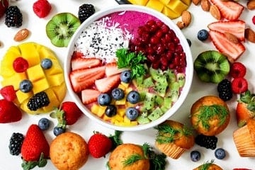 Purple smoothie bowl topped with various fruits, surrounded by an arrangement of colourful fruit.