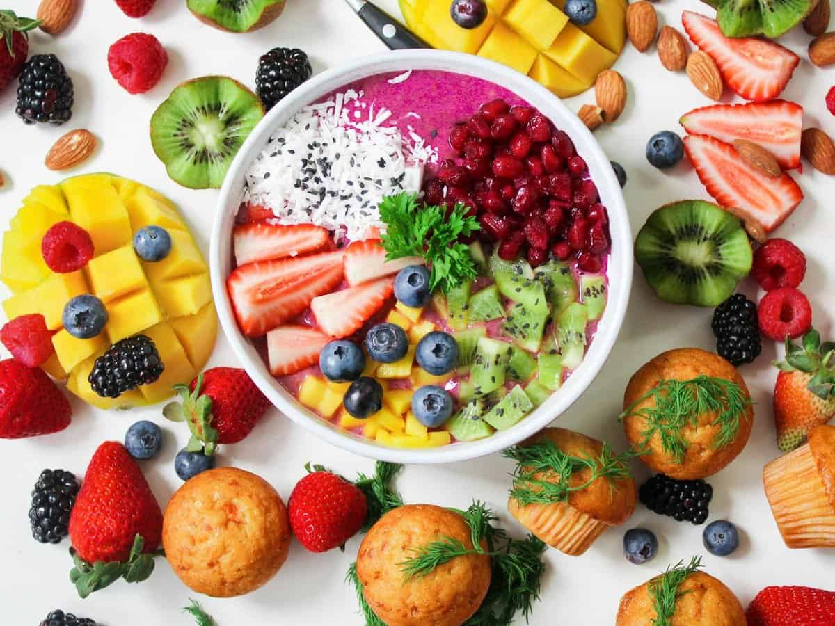 Purple smoothie bowl topped with various fruits, surrounded by an arrangement of colourful fruit.